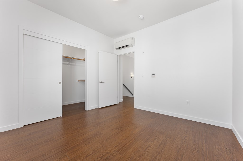 A room with white walls and wooden floors with a door on the left.